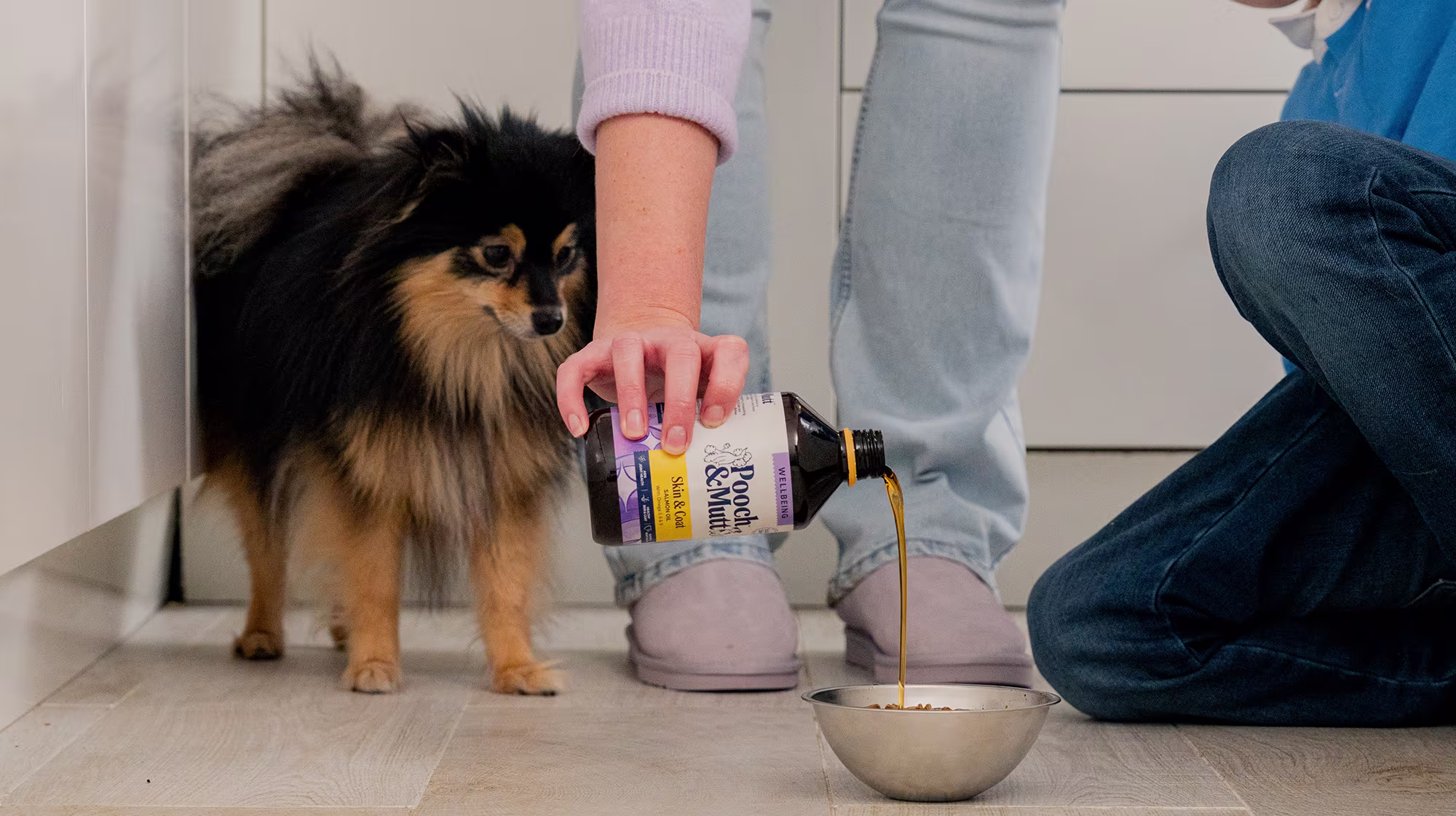 A black and tan Pomeranian stares at their bowl whilst their own pours Pooch & Mutt Salmon Oil over their kibble.